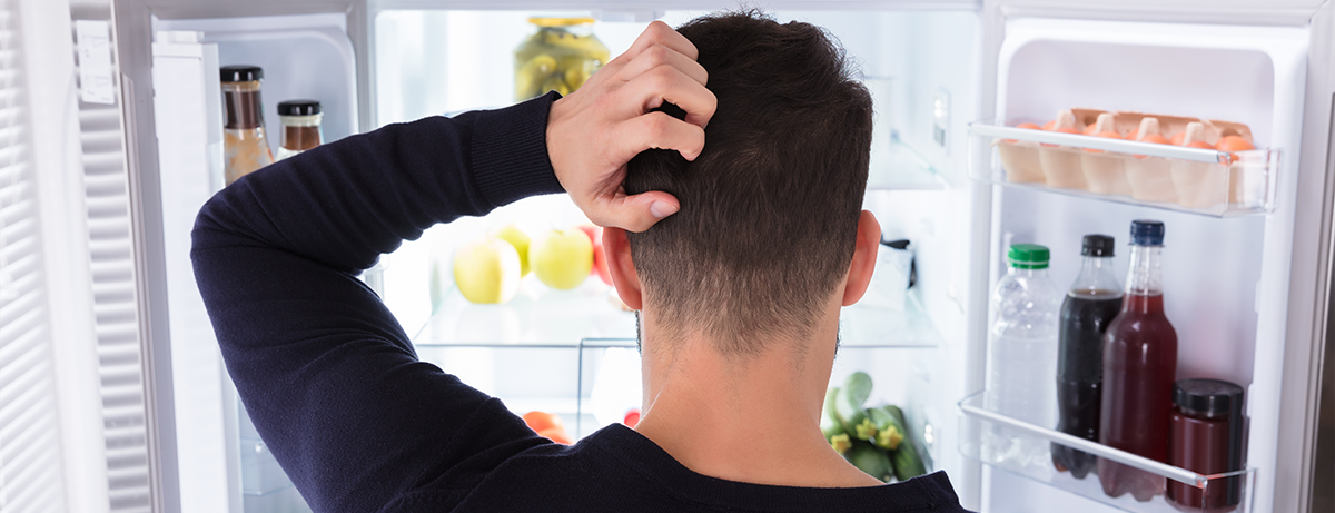 man scratching head in front of refrigerator