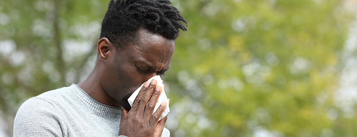 black man sneezing into a tissue outside