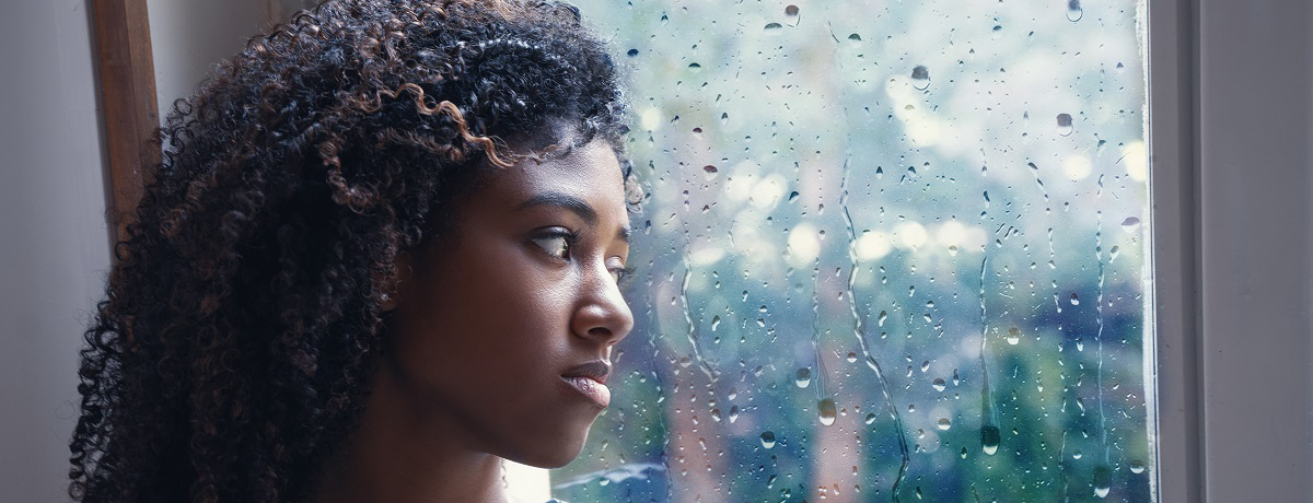 sad young black woman looking out window at rain