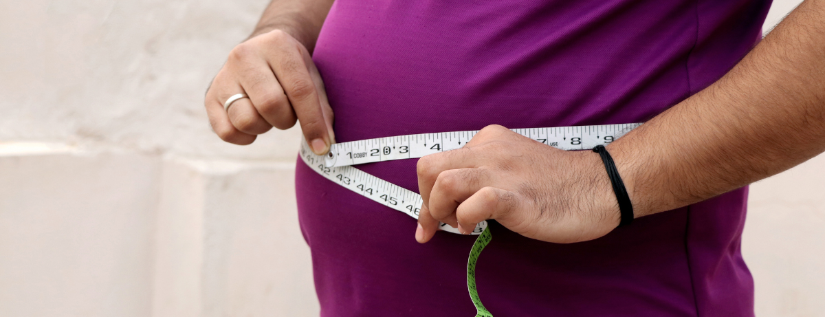 Man measuring his belly wearing a purple shirt